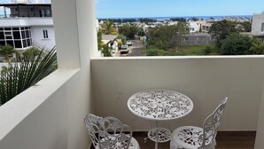 A balcony with a white table and chairs, overlooking a residential area with houses and a clear sky. - J'Vais Residence Flic en Flac (Flic en Flac)