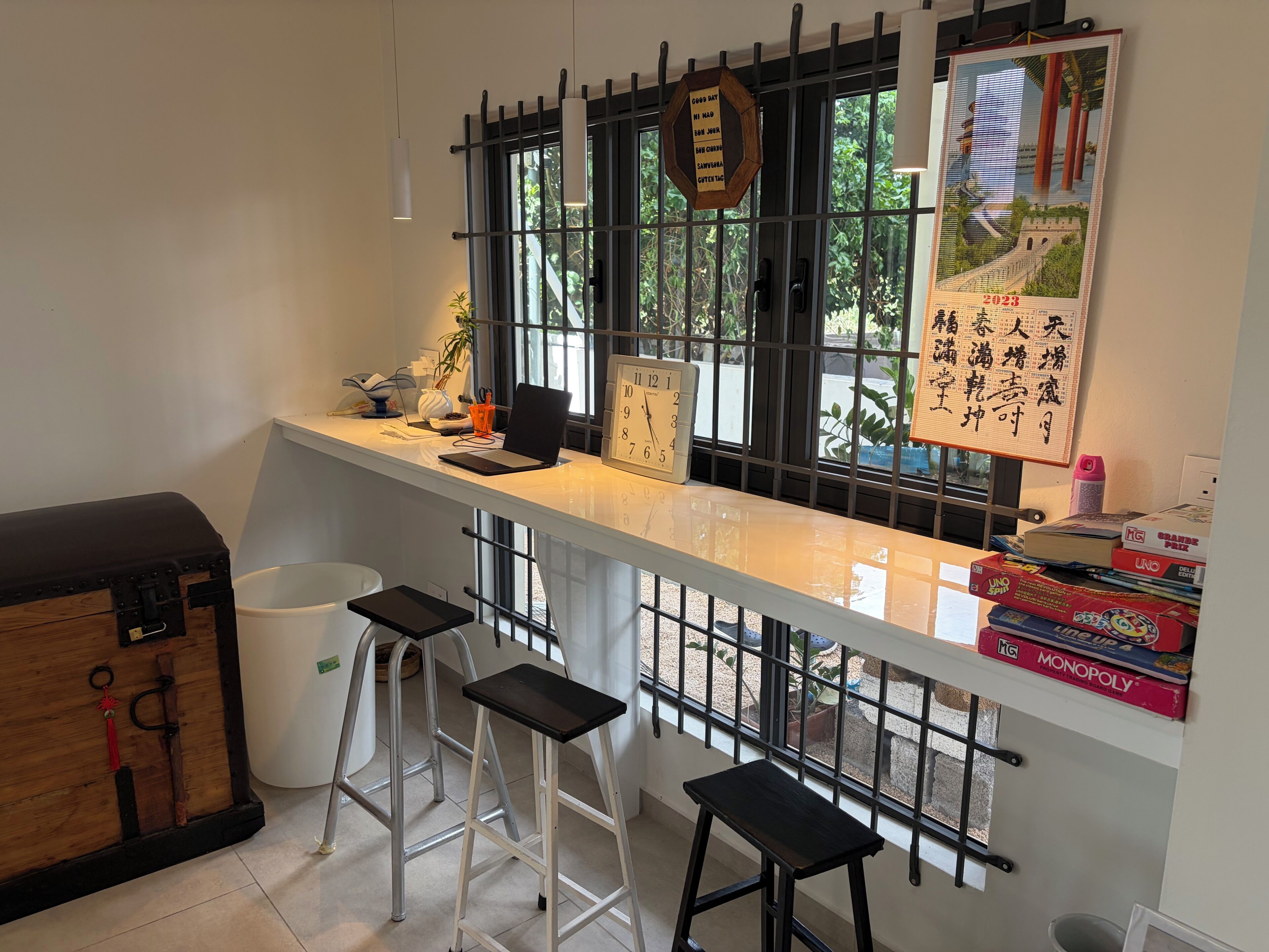 A kitchen with a white countertop, a laptop, a clock, and a window with a view of greenery.