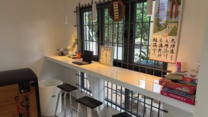 A kitchen with a white countertop, a laptop, a clock, and a window with a view of greenery. - J'Vais Residence Flic en Flac (Flic en Flac)
