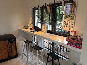 Una cocina con encimera blanca, una computadora portátil, un reloj y una ventana que ofrece vistas al verdor.