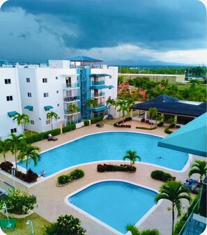 A hotel with a swimming pool, palm trees, and a view of the surrounding landscape. - “ Enjoy Your Coffee with Poolside Views at Harmony II – Balcony Bliss" (Santiago de los Caballeros)