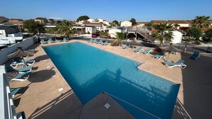 A swimming pool with lounge chairs and umbrellas, surrounded by houses and a wooden deck.
