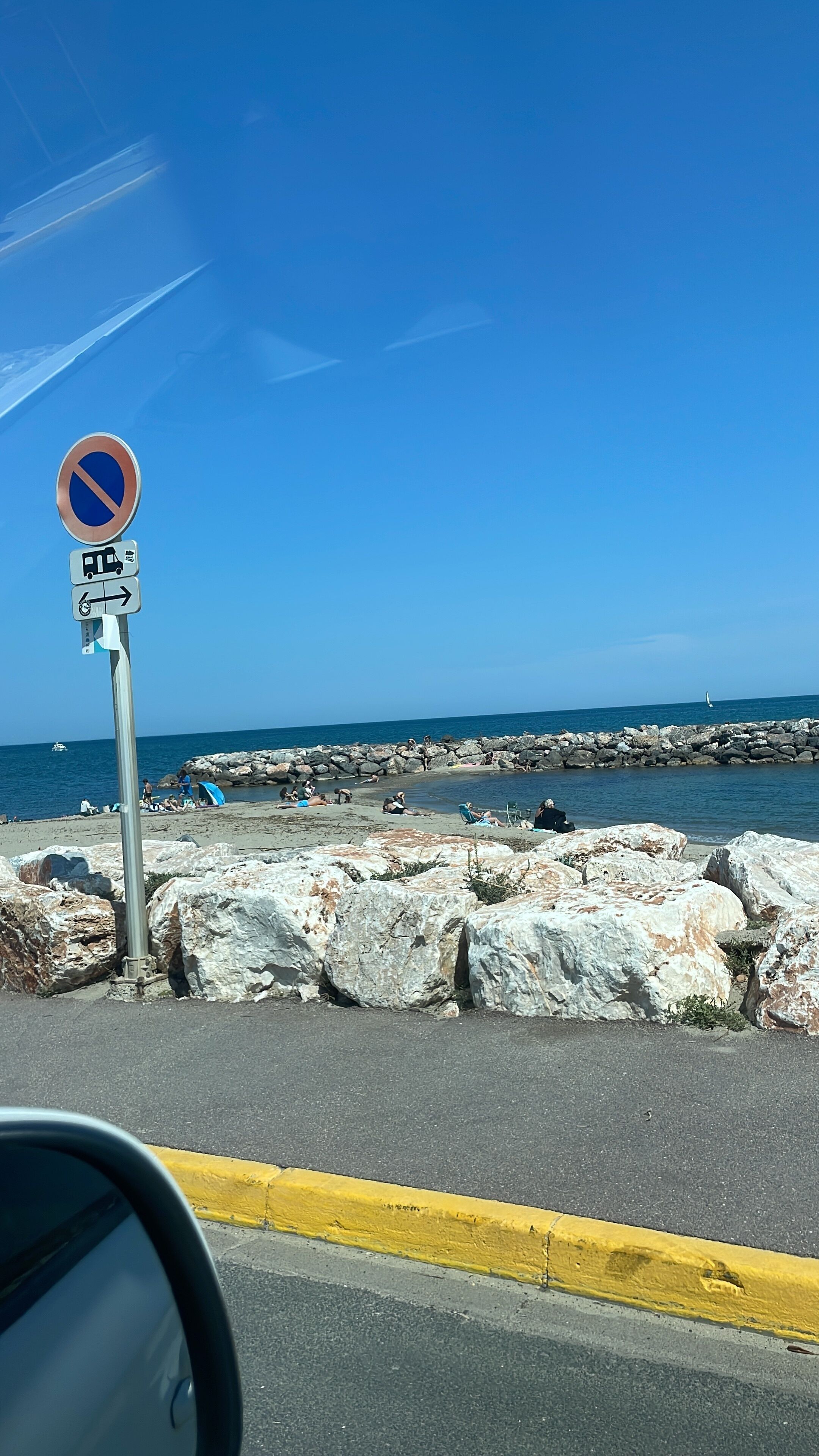 Une route côtière, un panneau indiquant l’interdiction de se garer, une digue rocheuse et un ciel bleu dégagé.