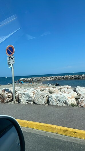Eine Küstenstraße mit einem Verbotsschild, einem felsigen Wellenbrecher und blauem Himmel.