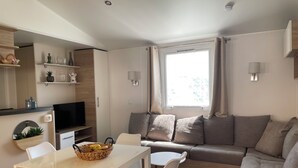 A modern living room with a sofa, a dining table with chairs, a TV, and a window with curtains.