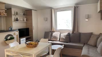 Una sala de estar moderna con un sofá, una mesa de comedor con sillas, un televisor y una ventana con cortinas.