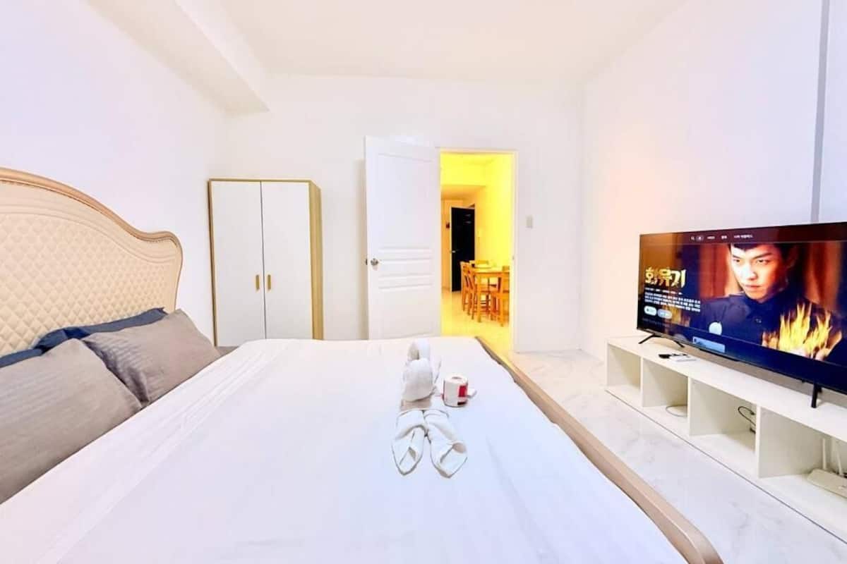 A hotel room with a bed, a TV, a wardrobe, and a door leading to a dining area.