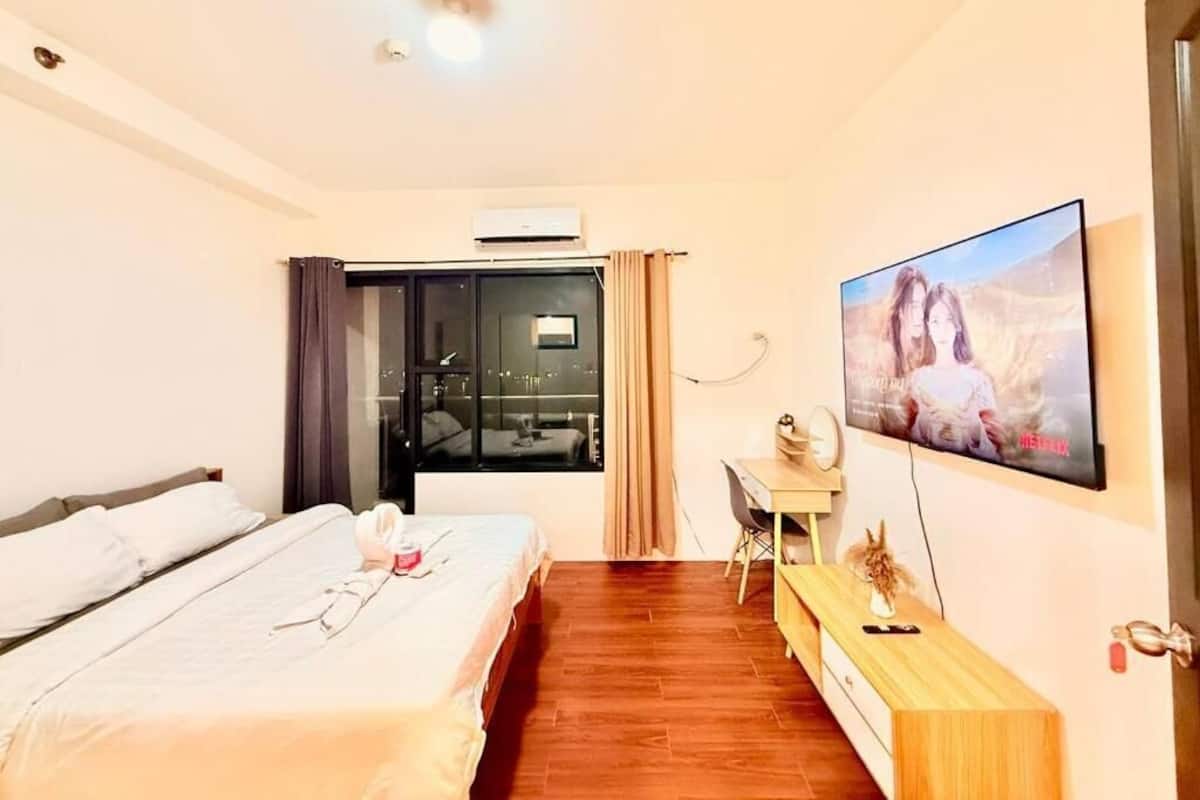 A hotel room with a bed, a desk, a TV, and a sliding door leading to a balcony.
