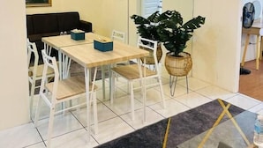 Un comedor moderno con un panel de vidrio, sillas blancas, una mesa de madera y una planta grande en maceta.