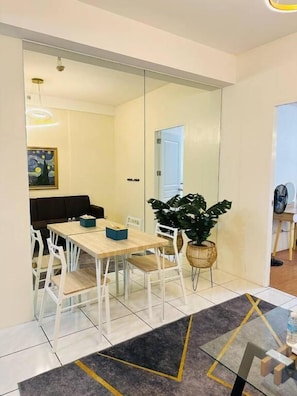 Un comedor moderno con un panel de vidrio, sillas blancas, una mesa de madera y una planta grande en maceta.
