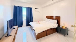 Una habitación de hotel con cama, escritorio, mesita de noche, lámpara y ventana con cortinas.