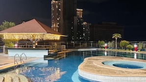 Una piscina con un hidromasaje circular, un pabellón cubierto y altos edificios al fondo.