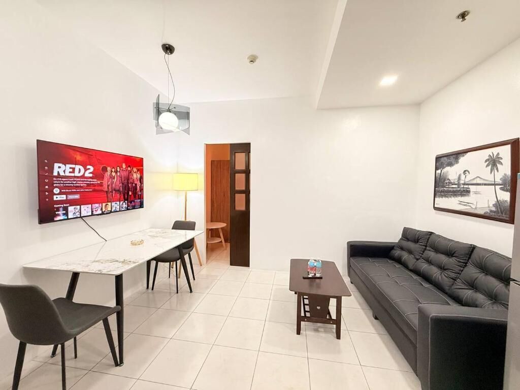 Una sala de estar moderna con televisor, sofá, mesa de comedor con sillas y una pequeña mesa auxiliar.