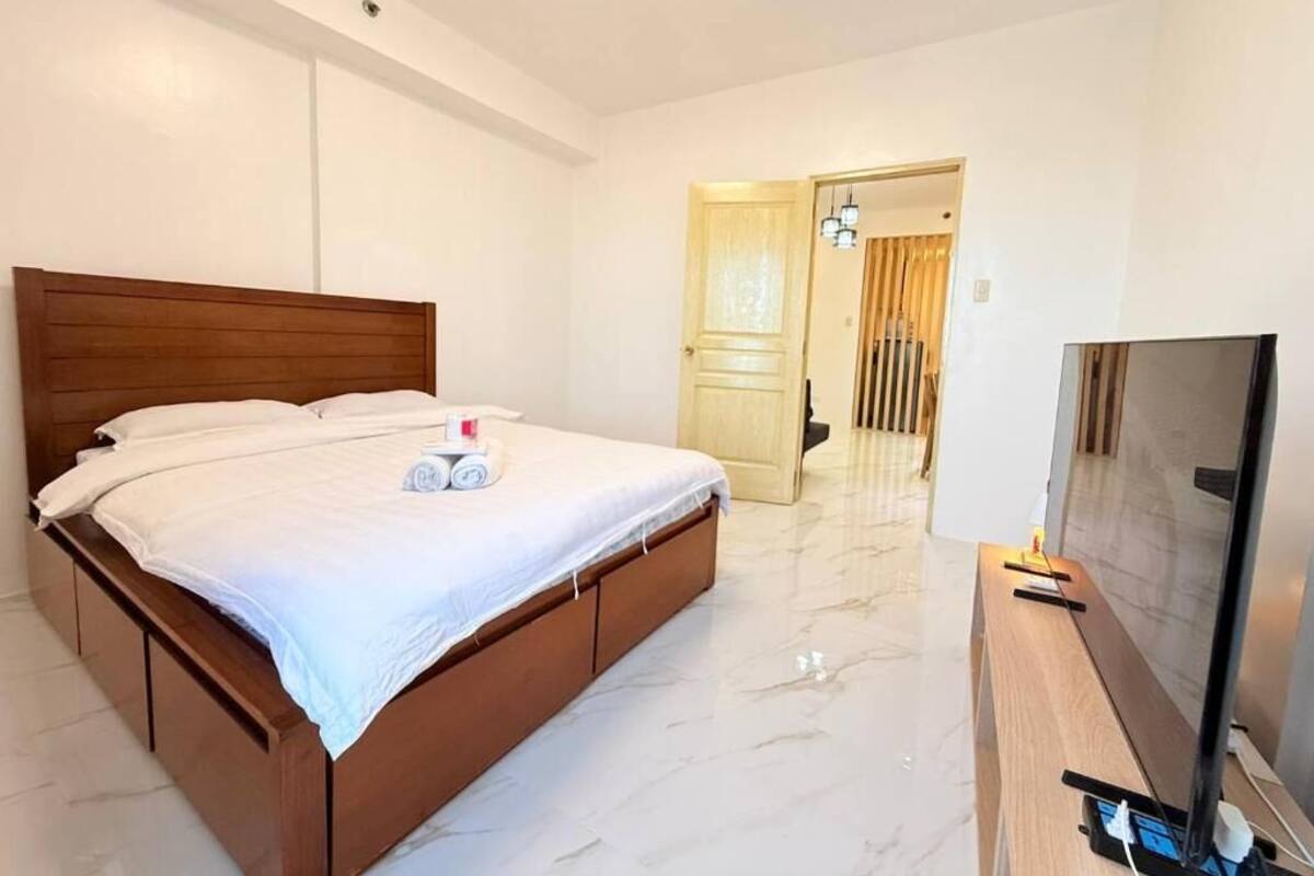 A bedroom with a wooden bed, a television on a stand, and a hallway leading to a door.