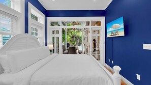 Un dormitorio con cama, televisor y vista a un jardín a través de un ventanal.