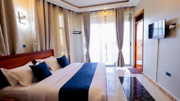 A hotel room with a large bed, curtains, a television, and a view of the outdoors. - Sea bridge view hotel mbarara (Mbarara)