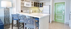 A compact kitchen with a central island, bar stools, a microwave, a refrigerator, and a green door. - 1 bedroom deluxe ocean view - Margaritaville Beach Resort - (Río Grande)