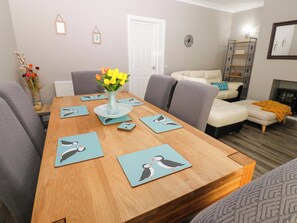 A dining area with a wooden table, grey upholstered chairs, and a vase with yellow flowers. - Amblers Rest (Morpeth)