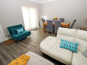 A living room with a teal sofa, a white sofa, and a dining area with a table and chairs. - Amblers Rest (Morpeth)