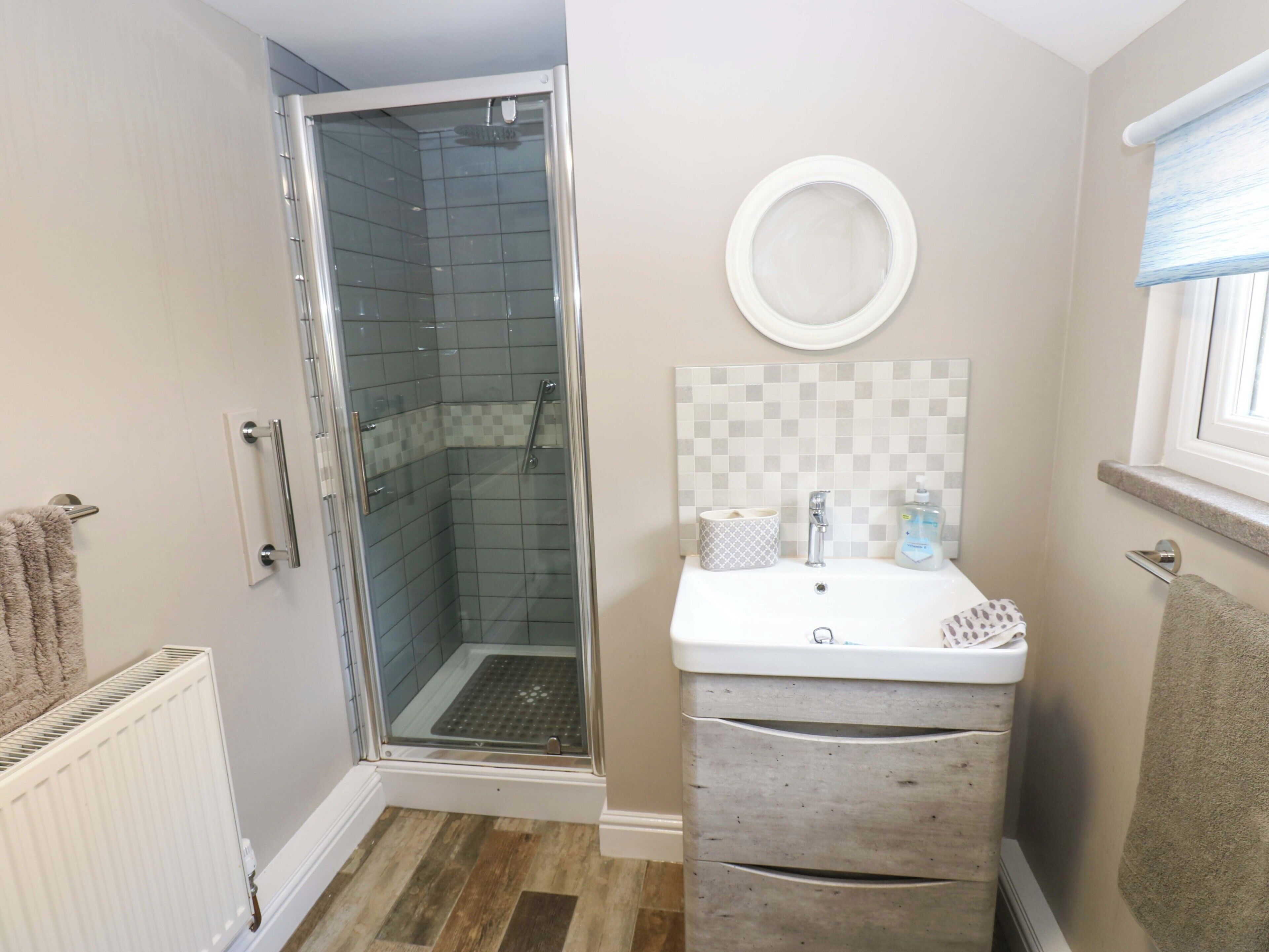 A bathroom with a glass shower enclosure, a white sink with a mirror above, and a towel rack.