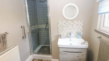 A bathroom with a glass shower enclosure, a white sink with a mirror above, and a towel rack.