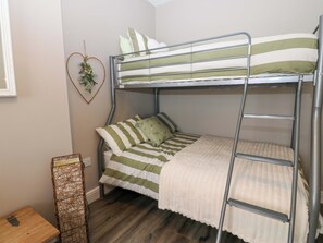 Uma cama beliche com roupa de cama verde e branca, uma decoração em formato de coração e uma cesta de vime.