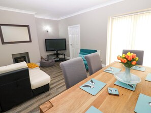 Uma sala de estar moderna com sofá, mesa de centro, televisão e canto de jantar com mesa e cadeiras.