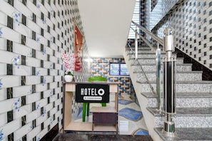 Un vestíbulo de hotel con un letrero 'HOTELO', una escalera y una pared con un diseño ornamental.