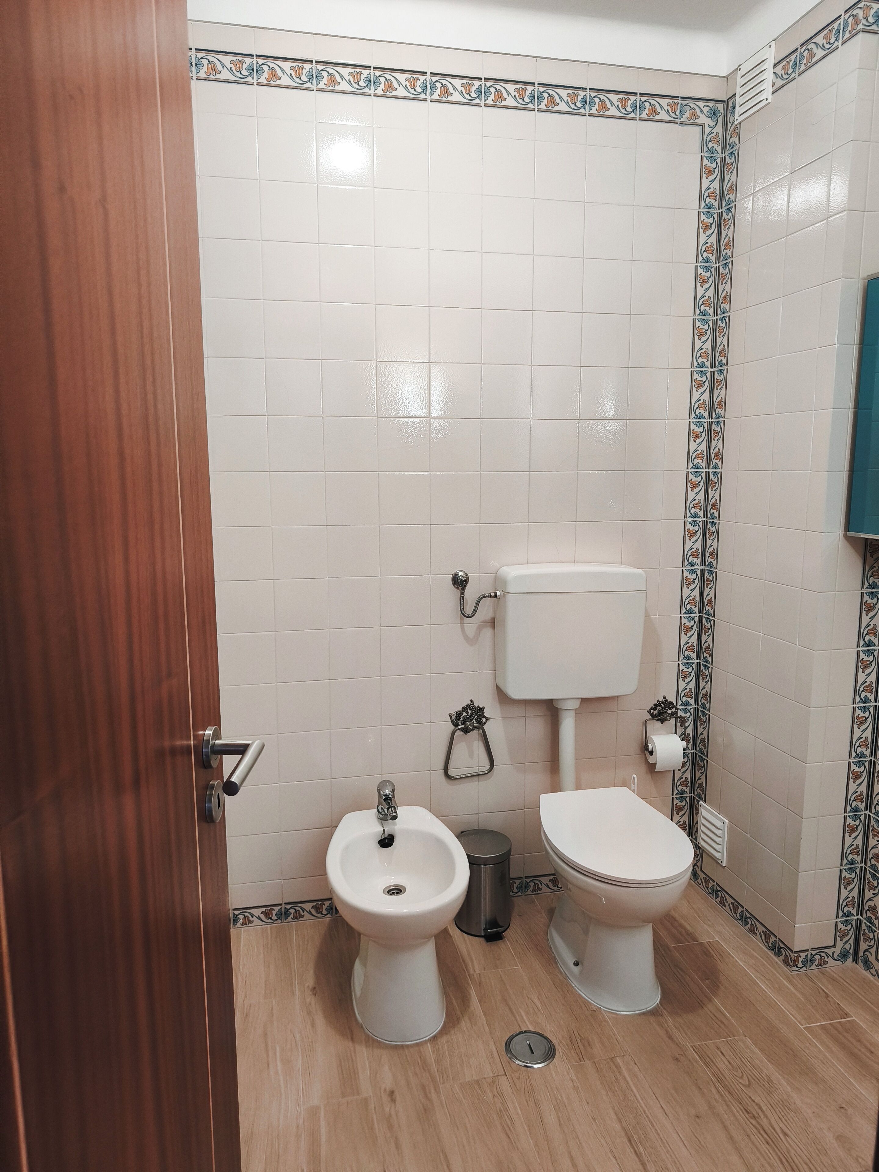A bathroom with a bidet, toilet, and a trash bin.