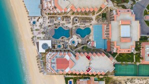 Vue aérienne d’un complexe hôtelier doté de plusieurs piscines, d’une plage et d’un court de tennis.