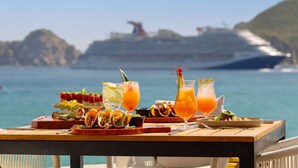 Une table garnie de nourriture et de boissons, un navire de croisière en arrière-plan et une vue dégagée sur la mer.