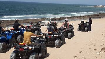 A group of people on ATVs on a beach with the ocean in the background.