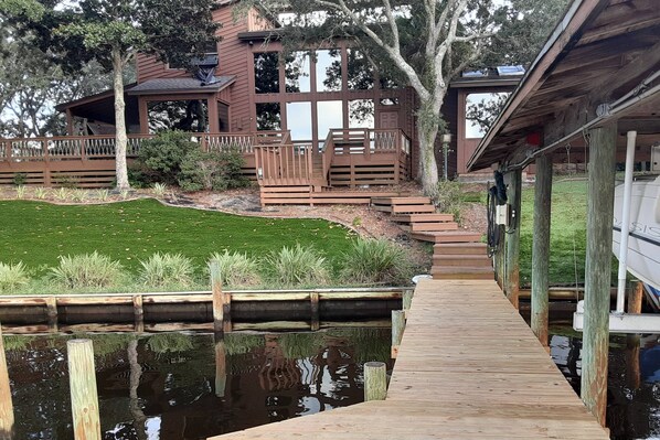 Eine hölzerne Mole, die zu einem Haus mit Terrasse und Teich führt.