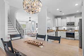 Una cocina moderna con armarios blancos, electrodomésticos de acero inoxidable y un comedor con mesa y sillas de madera.