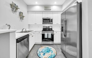 Una cocina moderna con armarios blancos, electrodomésticos de acero inoxidable y una alfombra con motivos de tortugas.