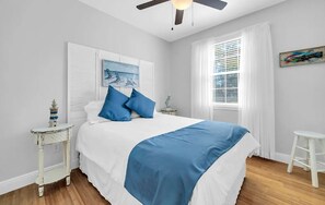 A bedroom with a bed, a ceiling fan, a window with curtains, a small table with a lamp, and a painting on the wall. - 🏖️Near the Beach | 4 Bikes | 30A | Pool | The Village 411🏖️ (Santa Rosa Beach)
