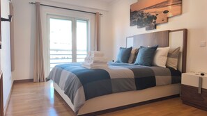A hotel room with a large bed, a view of the sea through the window, and a painting on the wall. - OLD TOWN, Apt. 110m2 on Avenida da Liberdade, AIR CONDITIONING/CAPBLE TV/FREE Wi-Fi (Albufeira)