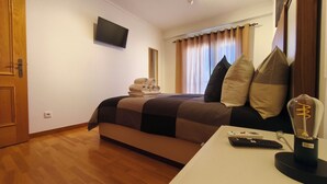 Ett hotellrum med en säng, en platt-TV som är monterad på väggen, ett nattduksbord med en fjärrkontroll och en lampa.