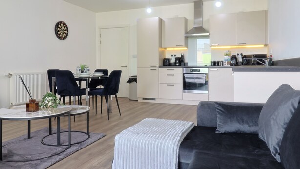 Una cocina moderna con armarios blancos, un comedor con mesa y sillas, y una sala de estar con sofá.