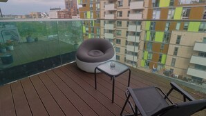Un balcón con barandilla de vidrio, una zona de estar circular, una mesita y una silla.