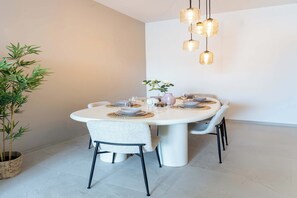 Ein Essbereich mit einem runden Tisch, gedeckt für vier Personen, einer Hängelampe und einem Blumentopf.