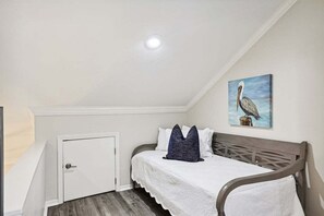 A bedroom with a bed, a door, a painting of a bird, and a sloped ceiling. - ☀️Renovated 3BR End-Unit~Golf Cart~Patio-Community Pool~Villa Bliss☀️ (Miramar Beach)