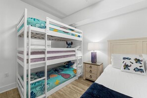Een stapelbed met meerdere planken, een nachtkastje met een lamp, en een bed met thematische kussens.