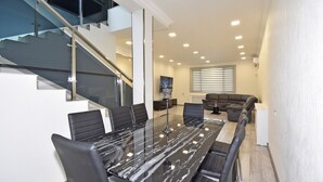 Una sala de estar moderna con una escalera de cristal, un comedor con mesa de mármol y una zona de estar con sofás.