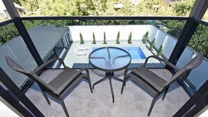 Un balcón con una mesa y sillas de vidrio, una pequeña piscina y vistas a un jardín con árboles.