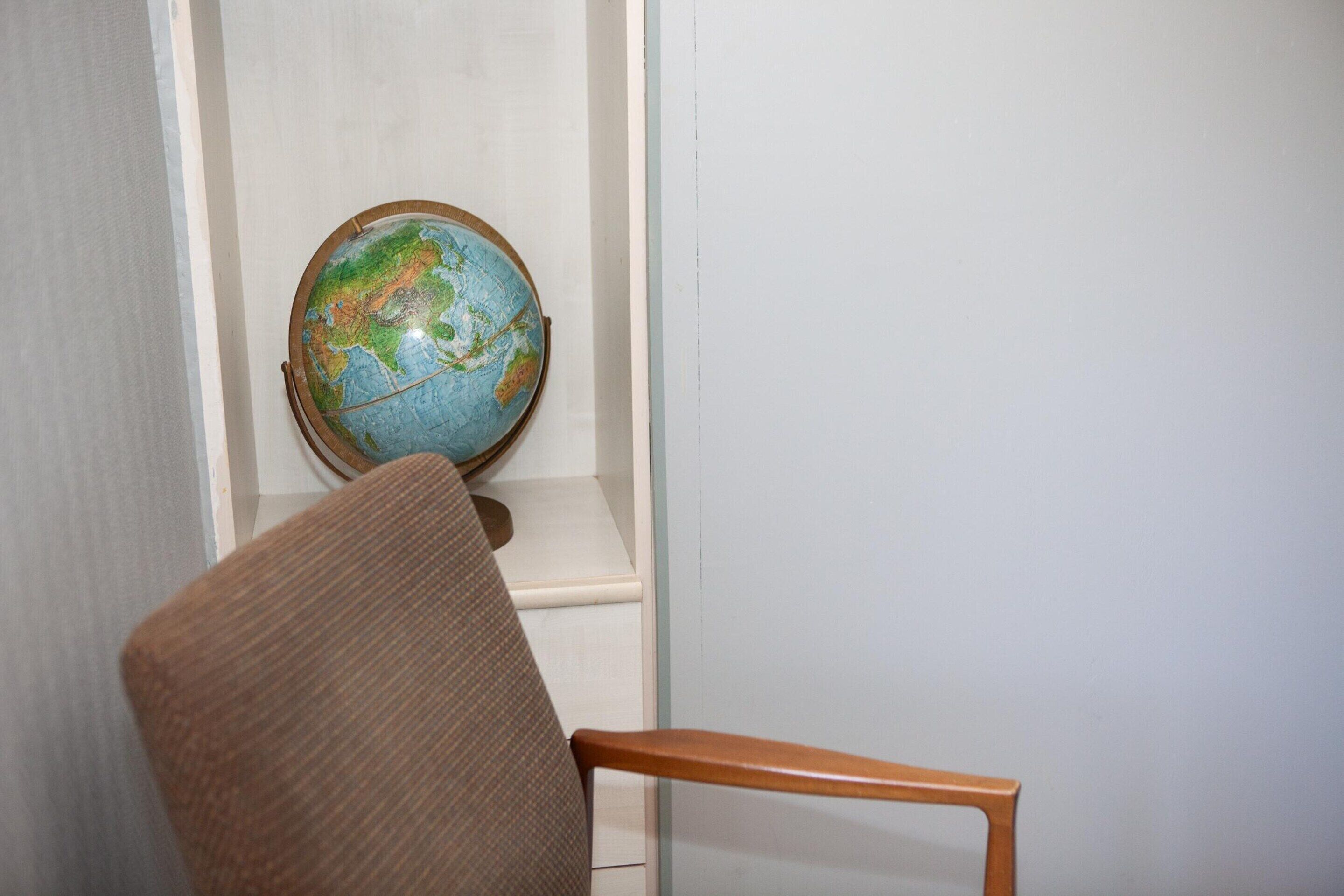 Una habitación con una silla de madera, un globo terráqueo en una estantería y una pared blanca.