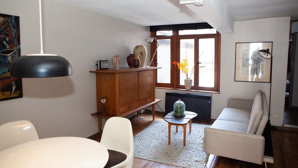 A living room with a sofa, a dining table, a cabinet, and a window with a view. - Holiday Stay in Center of Verviers (Verviers)