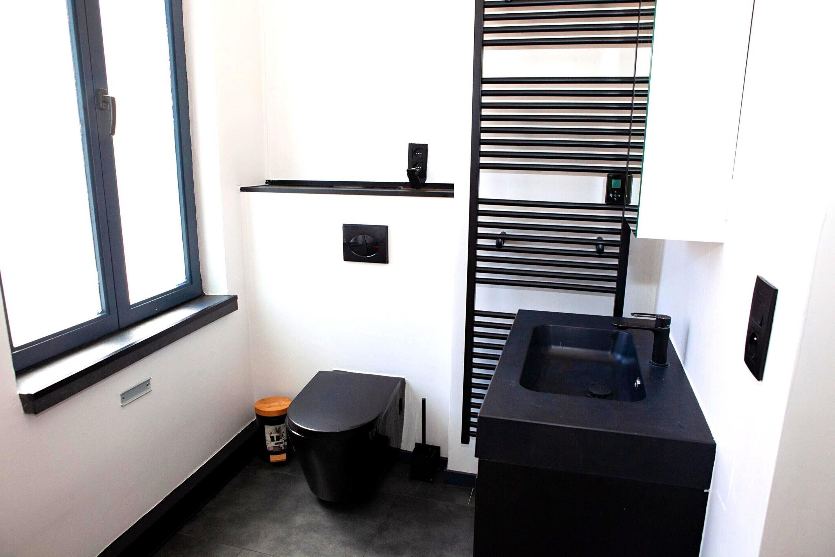 A compact bathroom with a window, a toilet, a sink, and a black towel rack.