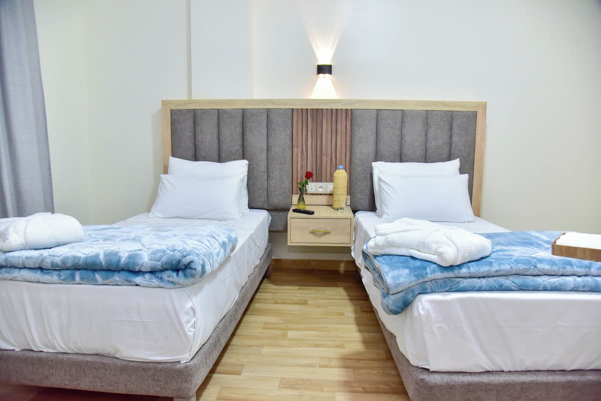 Quarto de hotel com duas camas, uma mesa de cabeceira com abajur e luminária na parede.