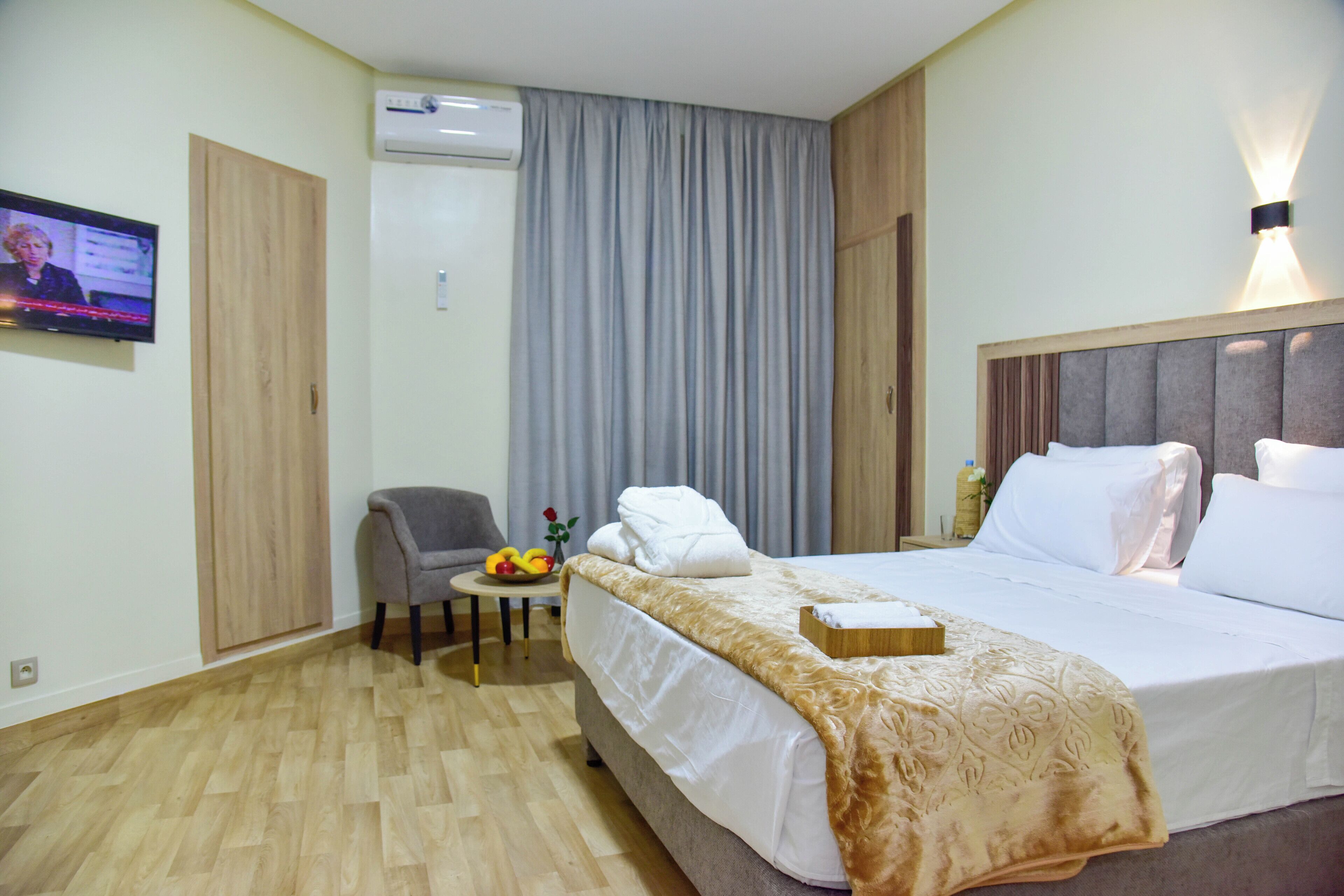Ein Hotelzimmer mit Bett, Sessel, kleinem Tisch mit Obst und Fernseher an der Wand.